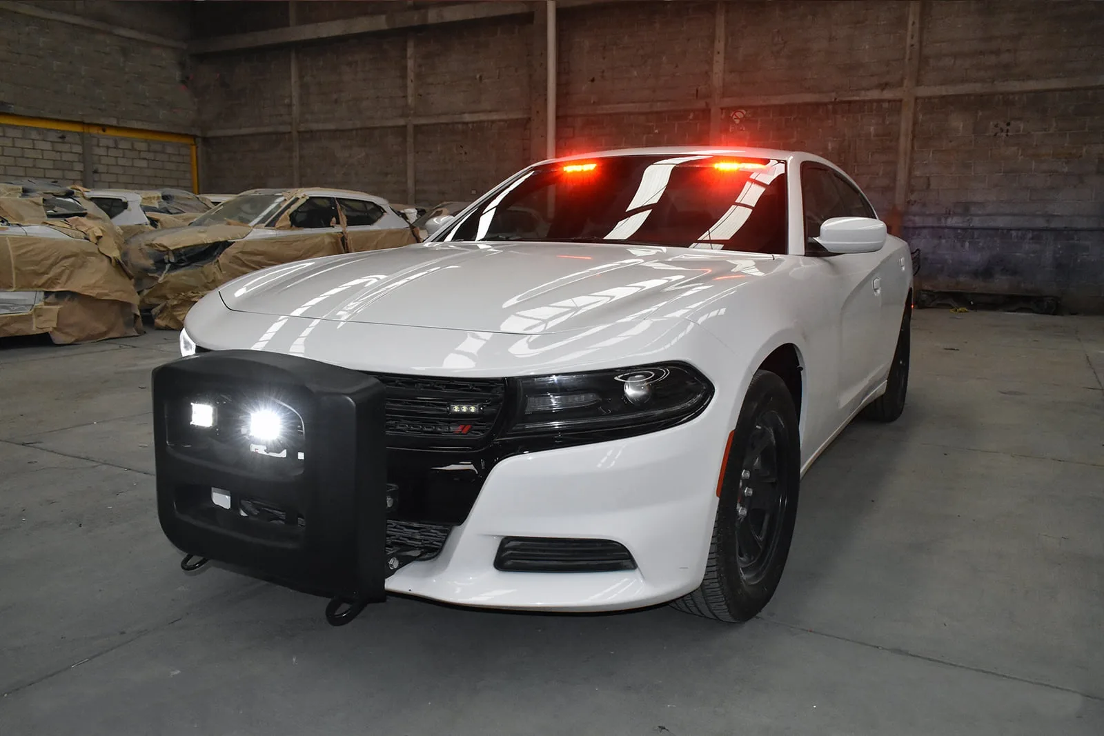 Patrulla sedán blanca con tumbaburro y luces encendidas en la nave